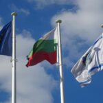 Three flags, including Bulgaria and EU, waving under a blue sky.