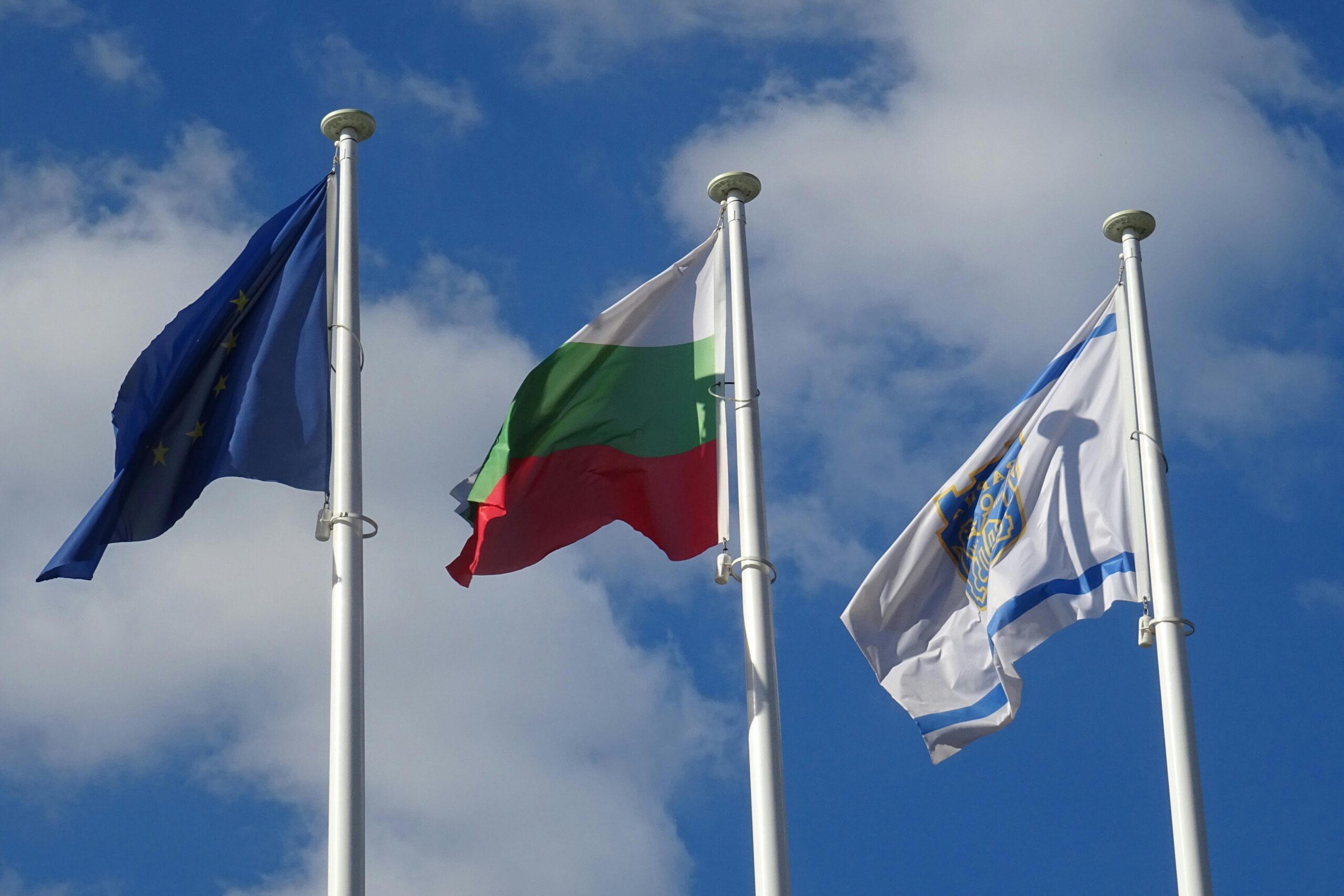 Three flags, including Bulgaria and EU, waving under a blue sky.